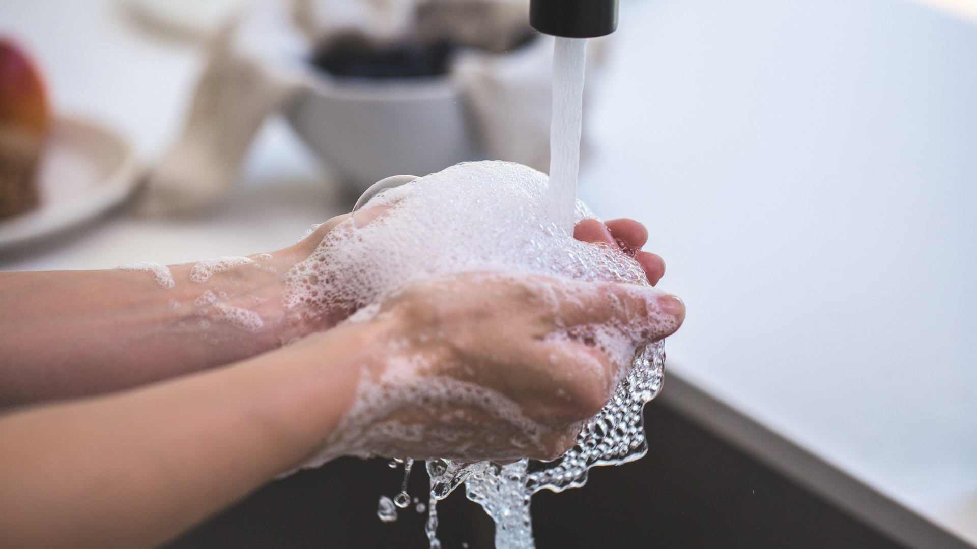 Mains savonnées rincées sous un robinet, hygiène à domicile.