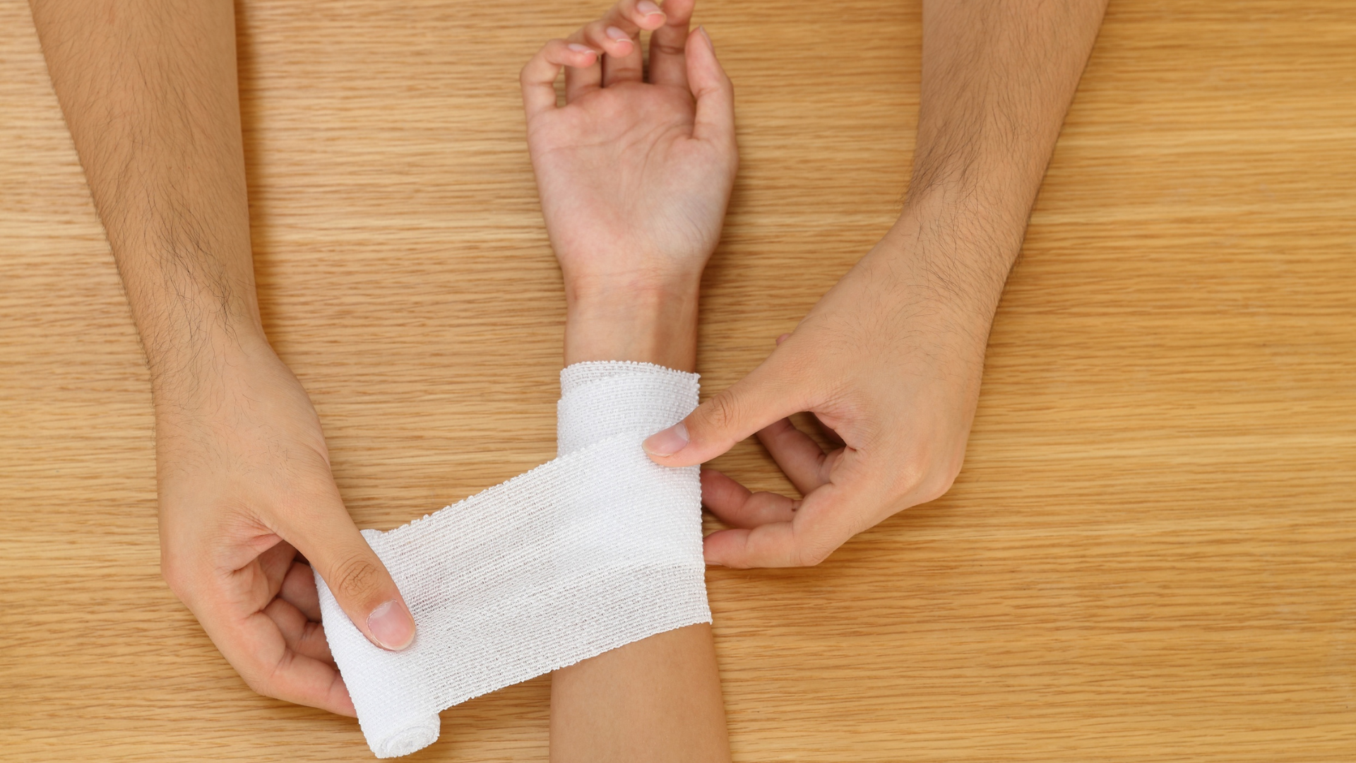 Pose d’un bandage au poignet sur table en bois, gros plan des mains.